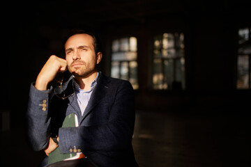 Portrait of businessman sitting on chair in empty room with thoughtful expression. Business closure, company crisis, overcoming difficulties