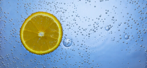 a slice of orange in blue water with bubbles. close-up. macro. cold lemonade