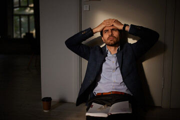 Portrait of young businessman sitting on floor in empty room. Business closure. Depression and...