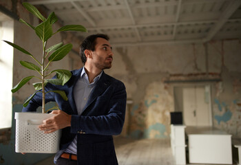 Portrait of young businessman walking out empty room with flower. Business closure. Depression and...