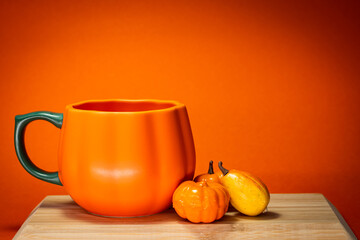Pumpkin shaped mug with orange background and ornaments on a small wood tray