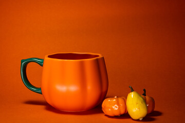 Pumpkin shaped mug with orange background and ornaments