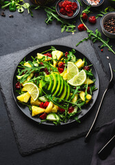 Fresh vegan salad with pineapple, arugula, avocado and dried cranberry on black stone kitchen table, top view. Healthy eating, clean diet food, weight loss concept