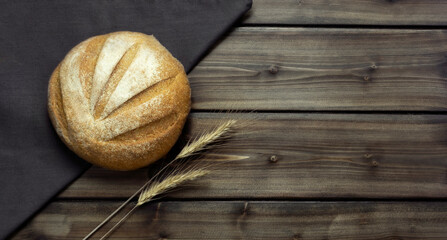 rye round bread on a gray napkin on a dark wooden background with spikelets of wheat with a copy space