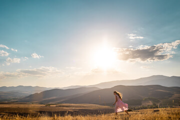 Obraz premium a girl in a pink dress walks across the field against the backdrop of mountains.