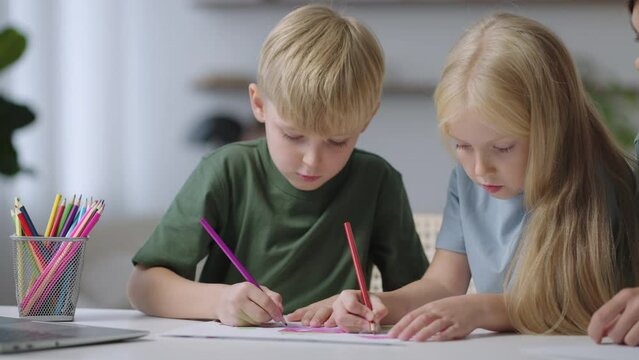 Two children draw together sitting at the table and mom helps. a boy and a girl draw together at a table