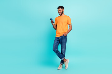 Fototapeta na wymiar Full length photo of good mood man dressed orange t-shirt typing samsung modern device empty space isolated turquoise color background