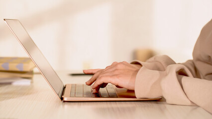 Cropped view of woman using laptop with blank screen at home.