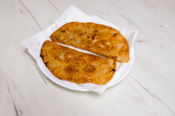 Homemade chebureks with filling and tomato sauce on a white background, close - up