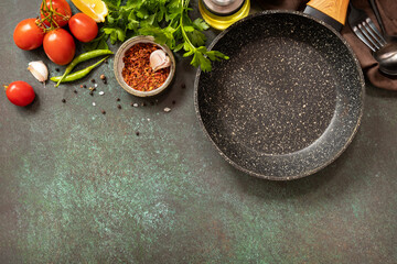 Food cooking background with Frying pan. Empty skillet, vegetables, spices and herbs on dark table background. View from above. Copy space.