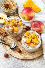 Healthy autumn or winter breakfast granola. Homemade dessert with yogurt, granola, caramel apples and pumpkin, cinnamon, nuts on a stone table. Copy space.