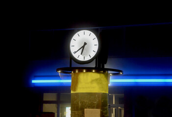 Naklejka premium clock above a cylinder-shaped poster surface with lighting. large public illuminated clock in the square by the bus station.