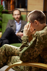 Young distressed woman in military uniform talking to psychologist during therapy session, indoors. Help, support, ptsd, health and harmony concept