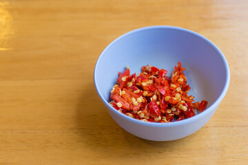 Chopped red chili put in a blue cup on the wooden table. It’s a spicy topping added with sukiyaki or shabu sauce.