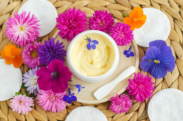 Obraz na płótnie Canvas Yellow facial mask (banana face cream, shea butter hair mask, body butter) and fresh purple flowers. Natural skin and hair care concept.