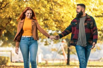 Young happy couple looking at each other while holding hands and walking in autumn park.