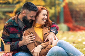 Young smiling couple relaxing in autumn leaves and hugging on a picnic.