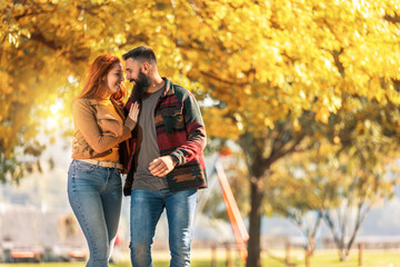 Fototapeta premium Young happy couple looking at each other while holding hands and walking in autumn park.