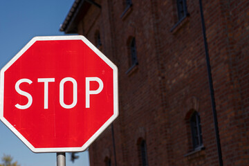 Ośmiokątny znak STOP ! Znak o wielokątnej tarczy i czerwonej barwie ( z białymi : napisem i oblamówką ) na tle budynku z czerwonej cegły . - obrazy, fototapety, plakaty