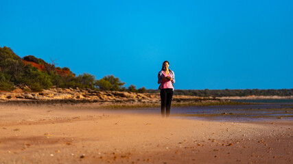 girl walks on red sand beach with red cliffs in the background, terra rosa in australia, holidays in western australia, francois peron national park