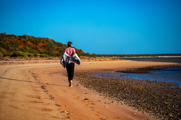 girl walks on red sand beach with red cliffs in the background, terra rosa in australia, holidays in western australia, francois peron national park