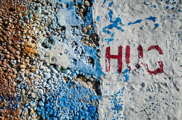 La parola hug scritta su un muro di cemento rovinato e con delle macchie di vernice blu 
