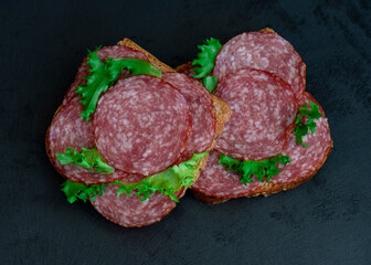 sliced ​​salami and lettuce. isolated on black background, top view. open sandwiches with sliced ​​salami sausage on rye bread