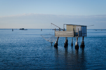 Un casone da pesca con una barca che passa visto dall'isola di Pellestrina in una giornata invernale