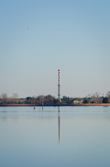 Obraz premium Una ciminiera bianca e rossa si riflette nell'acqua calma della laguna di Venezia vicino all'isola di Sant'Erasmo