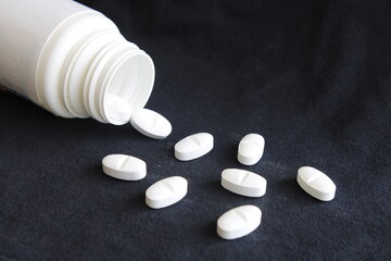 Botella de plàstico blanca con medicamento en pastillas para tratamientos de enfermedades volcadas sobre la mesa, forma un original diseño farmacèutico  con fondo negro