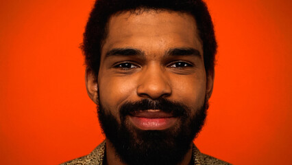 close up of smiling and bearded african american man isolated on orange.