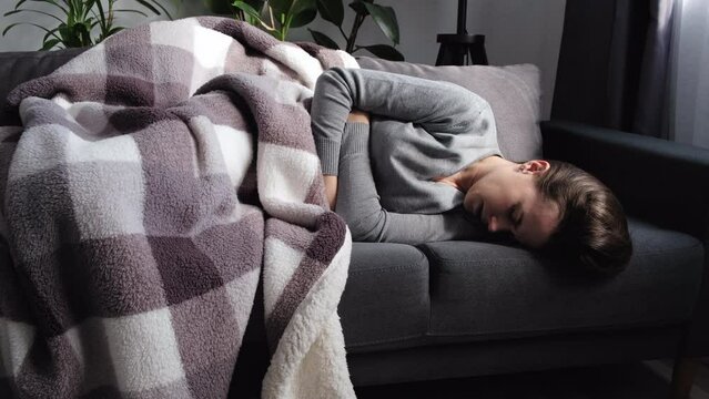 Sad unhappy young woman suffering from menstrual pain, feeling sick to stomach, holding belly, having abdominal cramps during period. Unhealthy female struggle with painful ache lying on couch at home
