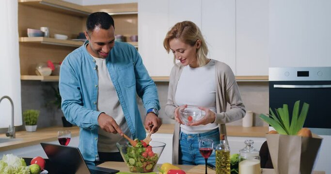 Happy attractive family cooking salad together at modern kitchen. African man and woman cutting and together cooking fresh natural vegetables and cooking for healthy lunch.