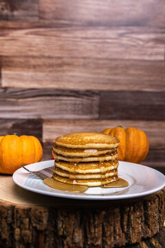 A stack of pumpkin pancakes with maple syrup on a rustic wood slice with copy space