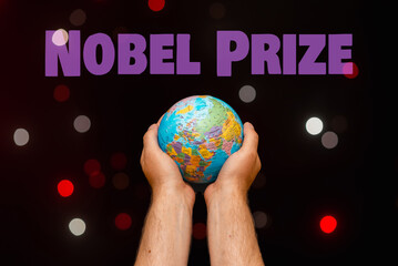 The inscription NOBEL PRIZE.A Man's hands hold a world globe in a darkness glowing small bubbles...