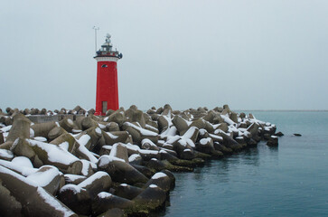 Il faro rosso di San Nicolò al Lido di Venezia con i frangiflutti coperti dalla neve in una fredda...