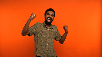 excited african american man with beard showing rejoice gesture on orange background.