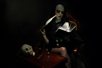 An emotional woman dressed for Halloween as a nun sits on a black background in an armchair with a notebook with a pen