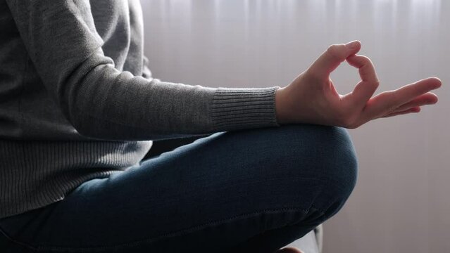 Close up of hand of young female sitting on comfy couch lotus pose, enjoy meditation do yoga exercise in living room at home. No stress, healthy habit, mindfulness lifestyle, anxiety relief concept