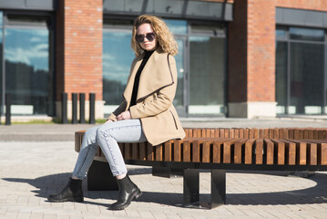 Portrait of a young Caucasian girl in a coat who is sitting on a bench.