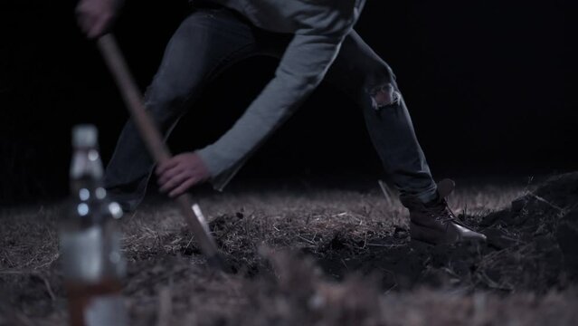 Criminal digs hole at night Young scary man digs hole in field. Close up of legs.