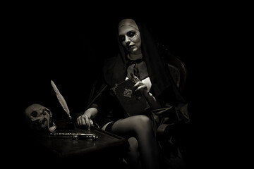An emotional woman dressed for Halloween as a nun sits on a black background in an armchair with a...