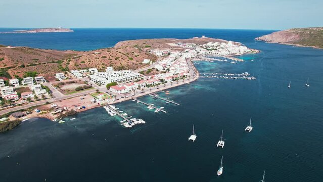 View from above of Fornells village located in a bay in the north of the Menorca 
Drone view of a harbour filled with llauts, the traditional Menorcan fishing craft, surrounded by white washed houses.