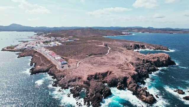View from above of Fornells village located in a bay in the north of the Menorca 
Drone view of a harbour filled with llauts, the traditional Menorcan fishing craft, surrounded by white washed houses.