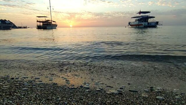 Morning on the beach in the village of Cirali, fishing nets lie on the yellow sand. Boats and ships in the distance of the Taurus mountain are moored near the shore. Landscapes of the Lycian Trail.