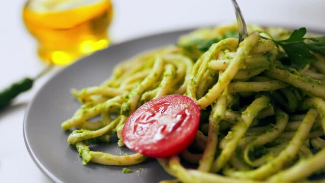 Green pasta cooked beautifully laid out on a plate, pasta large spaghetti green color hand picks up a fork red tomato on a plate with pasta beautiful ready meal meal cooking by a chef
