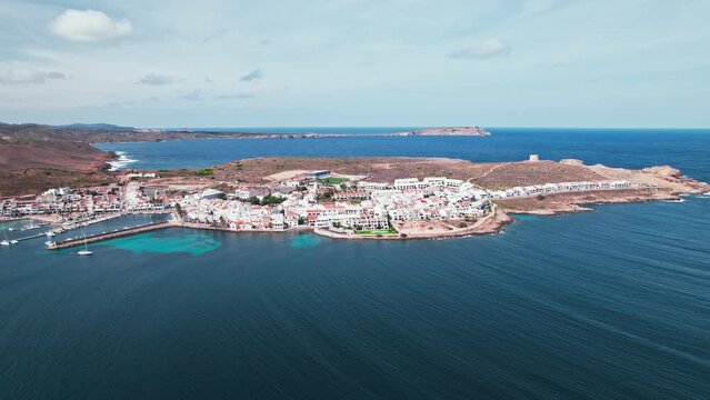 View from above of Fornells village located in a bay in the north of the Menorca 
Drone view of a harbour filled with llauts, the traditional Menorcan fishing craft, surrounded by white washed houses.
