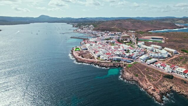 View from above of Fornells village located in a bay in the north of the Menorca 
Drone view of a harbour filled with llauts, the traditional Menorcan fishing craft, surrounded by white washed houses.