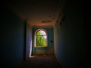 Obraz premium Abandoned hotel room with peeling blue wallpaper and green tree outside