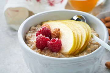 Oatmeal. Bowl of oatmeal porridge with raspberry, pear and honey on gray concrete old table background. Hot and healthy food for Breakfast, top view, flat lay